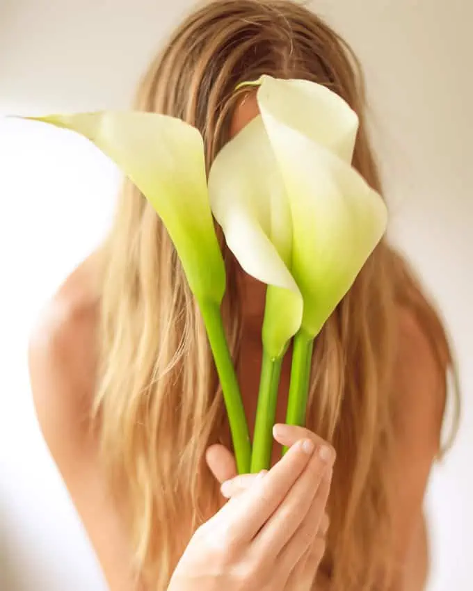 Frau mit blonden langen Haaren hält sich drei weiße Blumen vor das Gesicht