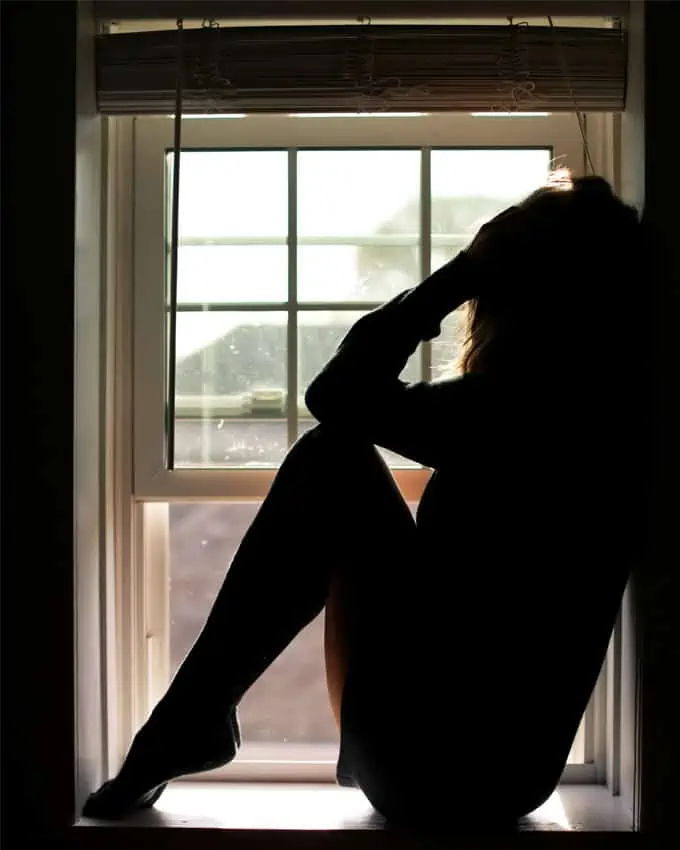 Ein trauriger Mensch sitzt auf der Fensterbank. Nur ihr schwarzer Schatten ist zu sehen