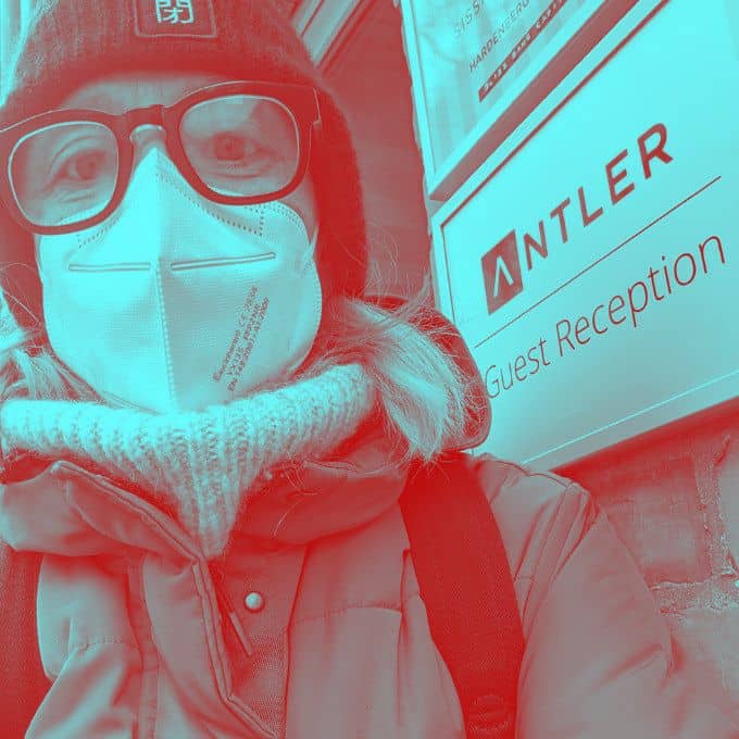 Frau mit Brille, Mütze und Maske in Winterjacke und Rollkragenpullover.