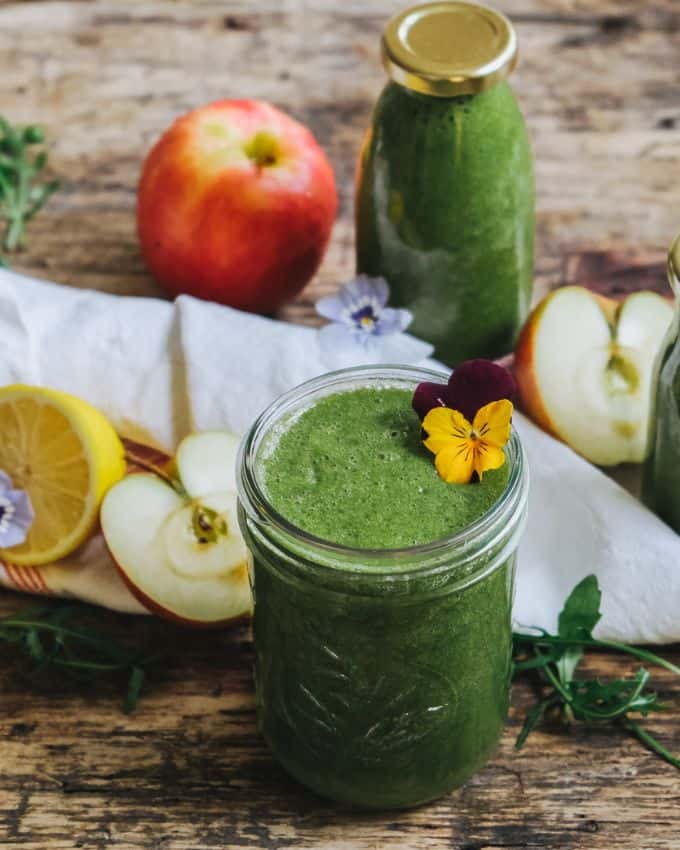 Green smoothie in glass with leaves and apples and lemon around it