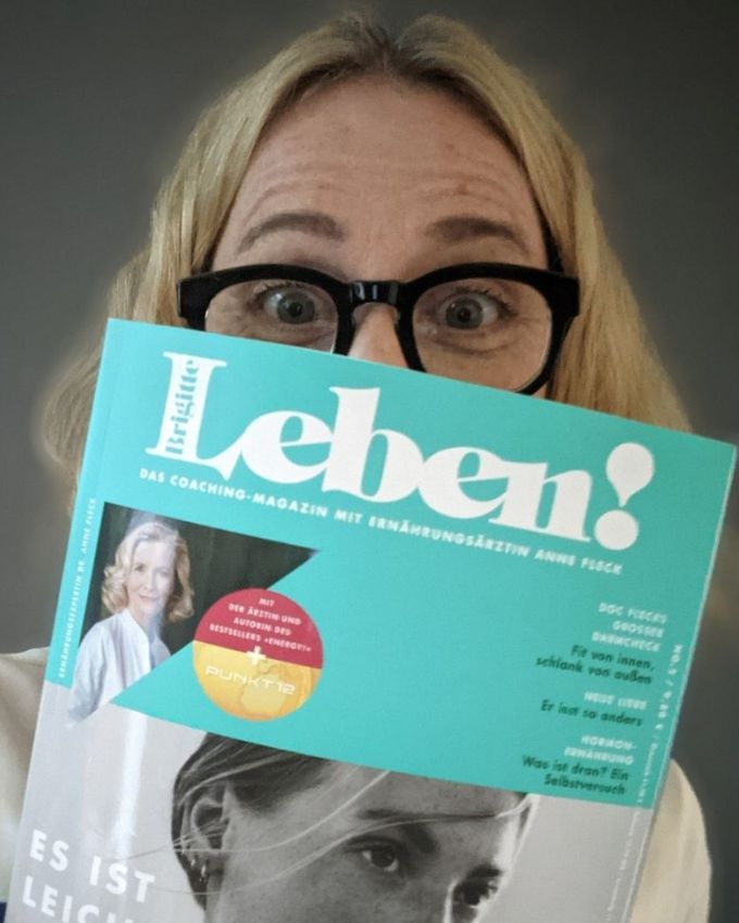 Frau mit blonden Haaren und schwarzer Brille hält "Leben!" Zeitschrift vors Gesicht.
