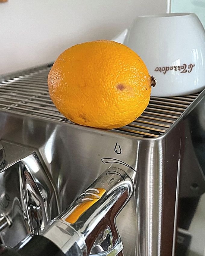 Silberne Kaffeemaschine auf der eine weiße Tasse steht und eine Zitrone liegt.