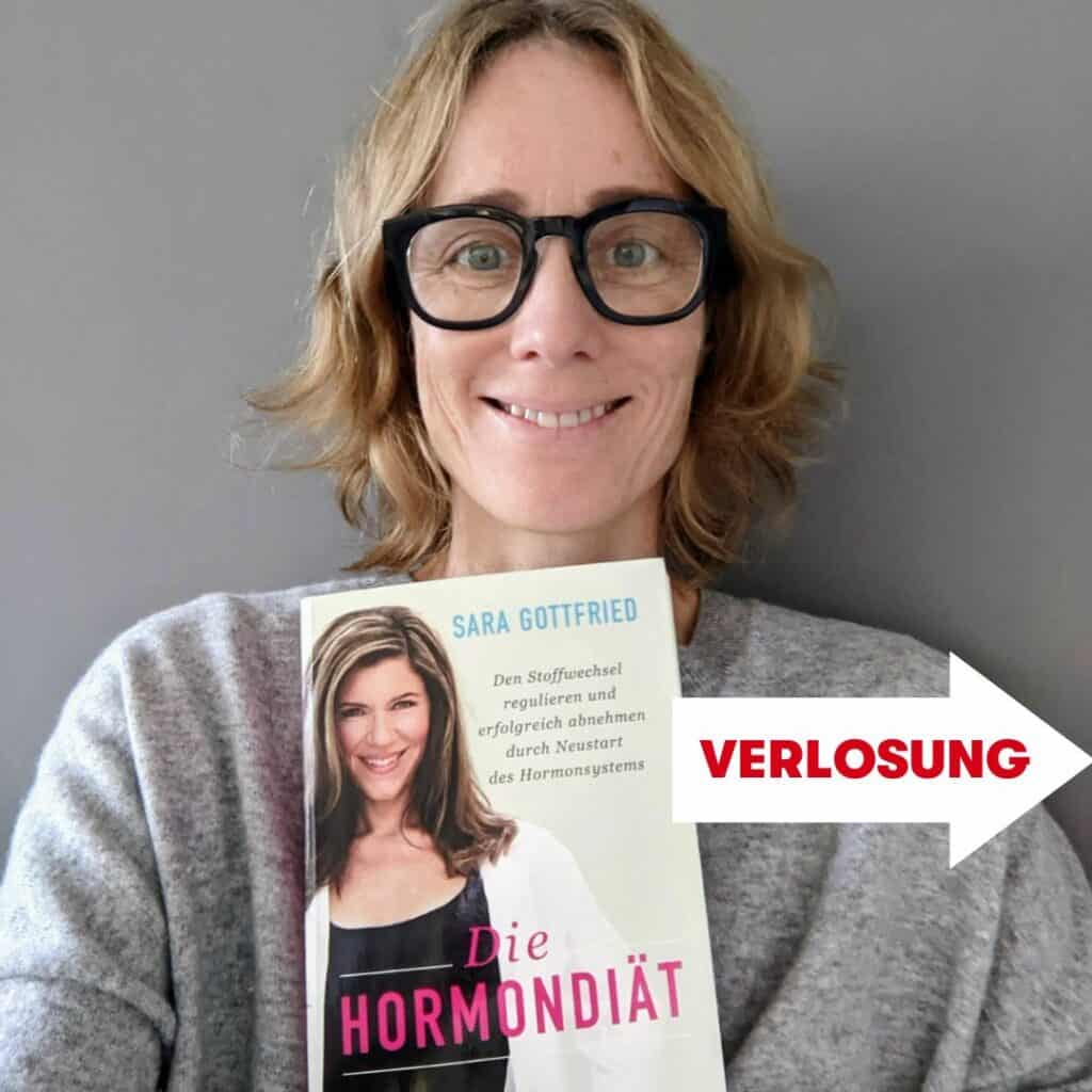 Lächelnde Frau mit schwarzer Brille hält das Buch "Die Hormondiät" vor sich, daneben steht auf einem Pfeil das Wort Verlosung.