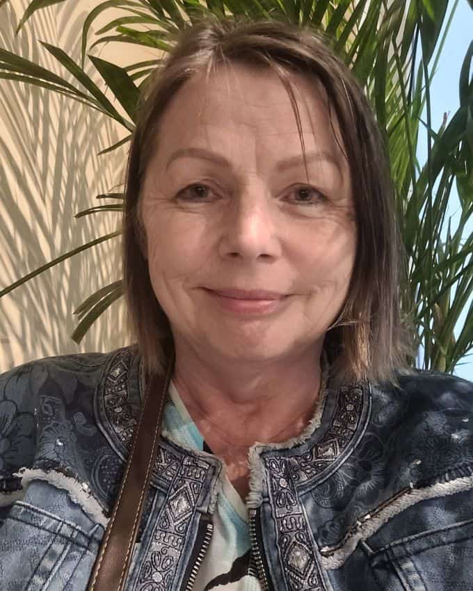 Selfie einer lächelnden Frau mit braunem Bob. Sie trägt eine Jeansjacke mit Strasssteinen und Stickborde. Über der rechten Schulter sieht man den dünnen, braunen Riemen einer Handtasche.