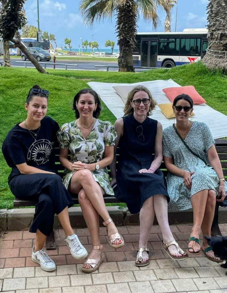 4 Frauen sitzen auf einer Parkbank in tel Aviv und lächeln in die Kamera