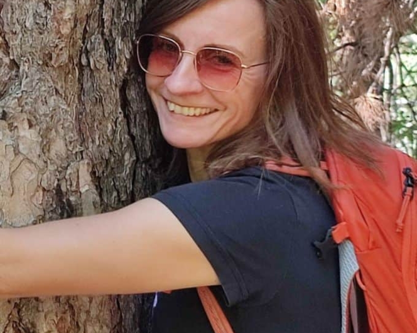 Eine Frau mit getönter Brille umarmt einen Baum.