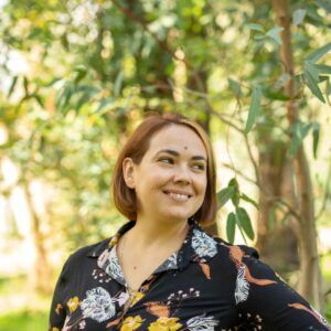 Marisa Tusha smiling with a green tree behind