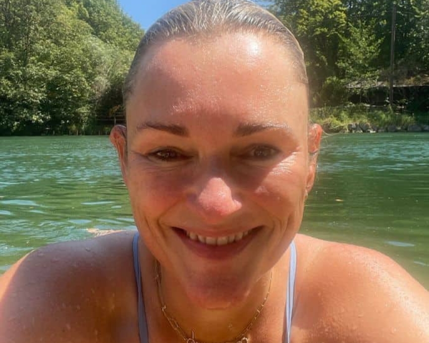 So sieht 49 aus. 49 jährige Frau schaut mit dem Oberkörper aus dem Wasser. Sue lächelt in die Kamera und trägt ein hellblaues Bikini Oberteil.