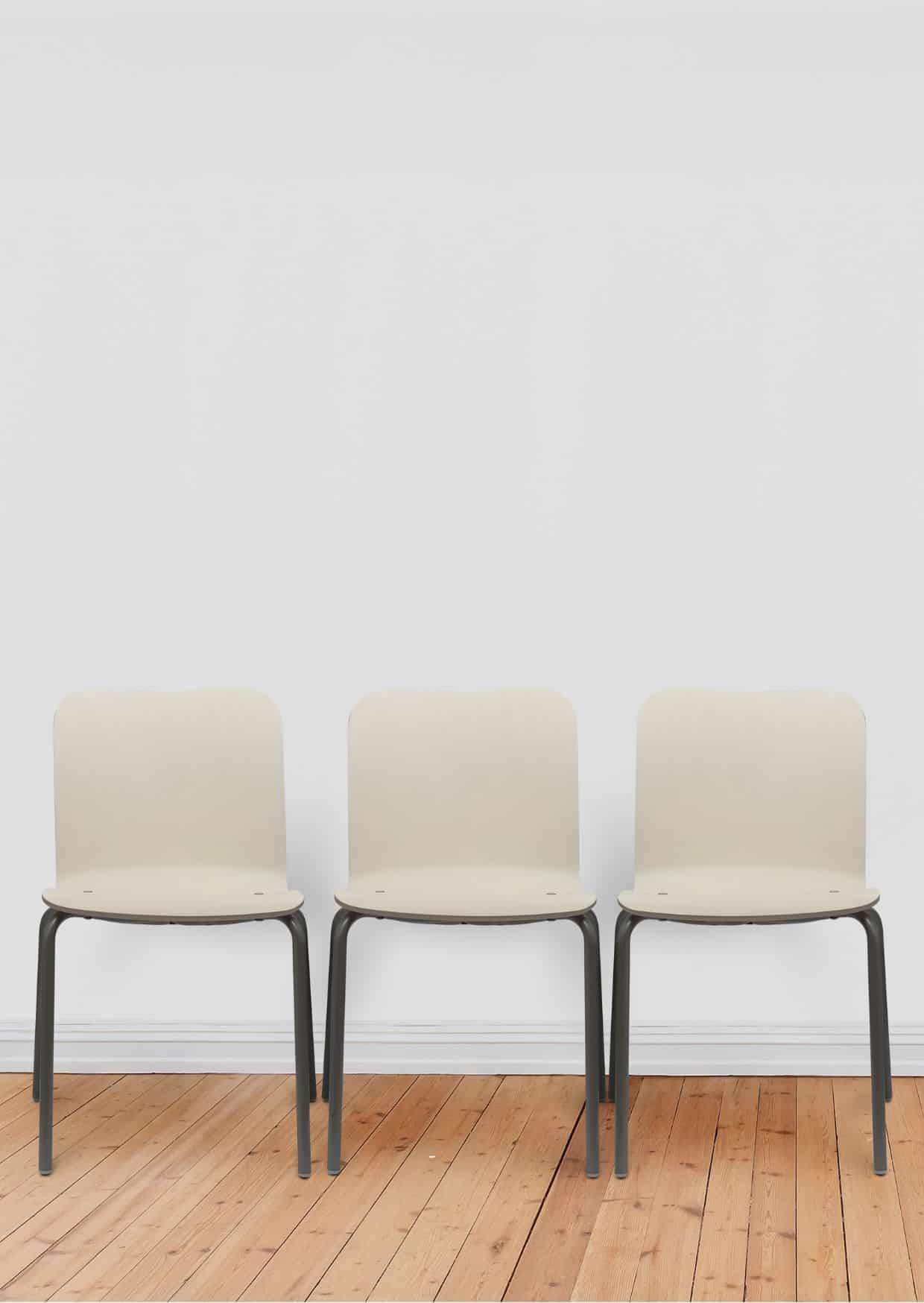three white chairs with black legs in front of a white wall. The floor is pine parquet.