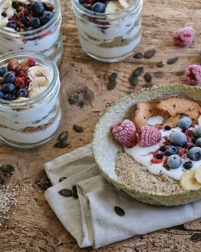A mixture of seeds, banana and fruit with yoghurt on a plate with a napkin underneath. It is on a wooden table