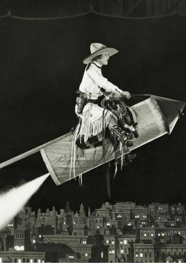Schwarz- weiß Foto eines Cowboys auf einer Rakete über eine Stadt fliegend