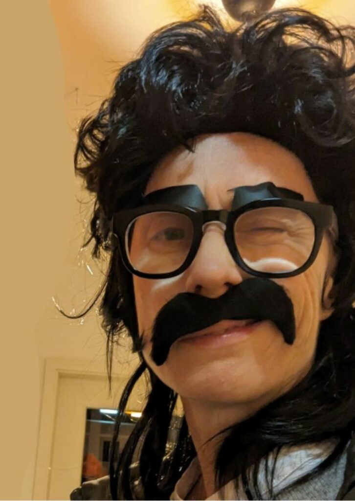 Frau mit schwarzer Kurzhaar Perücke und Brille mit angeklebtem Schnurrbart und Augenbraun