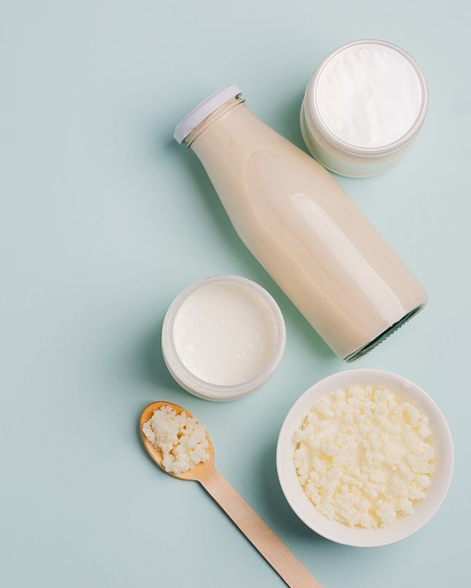 Milch in einer Glasflasche, zwei Gläser mit Joghurt, Holzlöffel mit Frischkäse