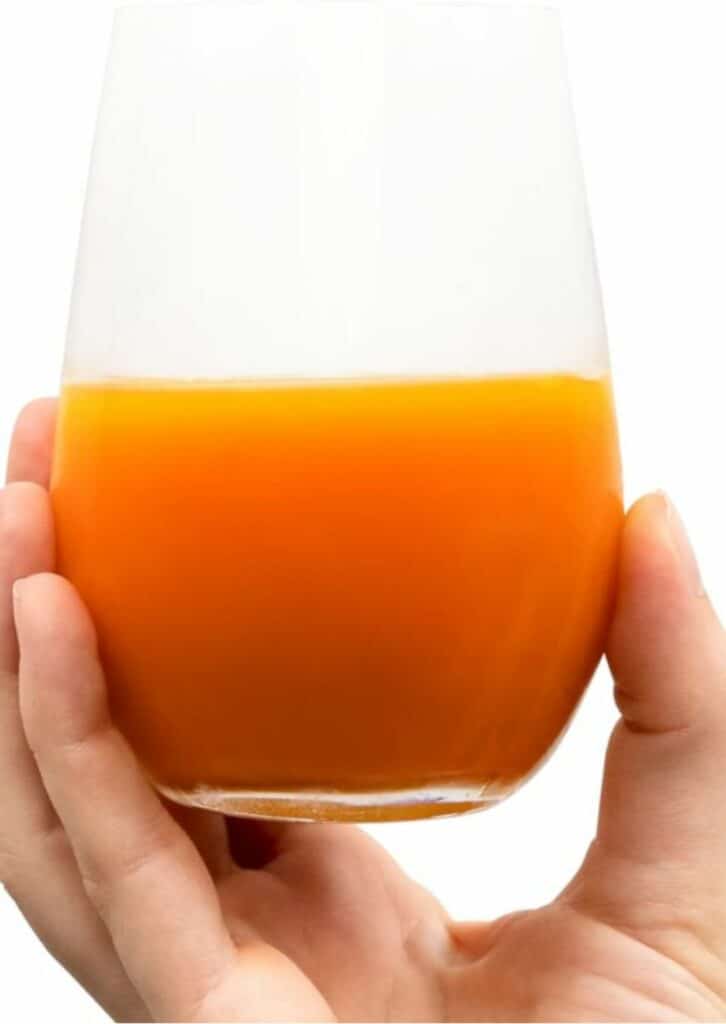 Eine Hand hält ein Glas mit orangefarbenem LaVita Mikronährstoffkonzentrat