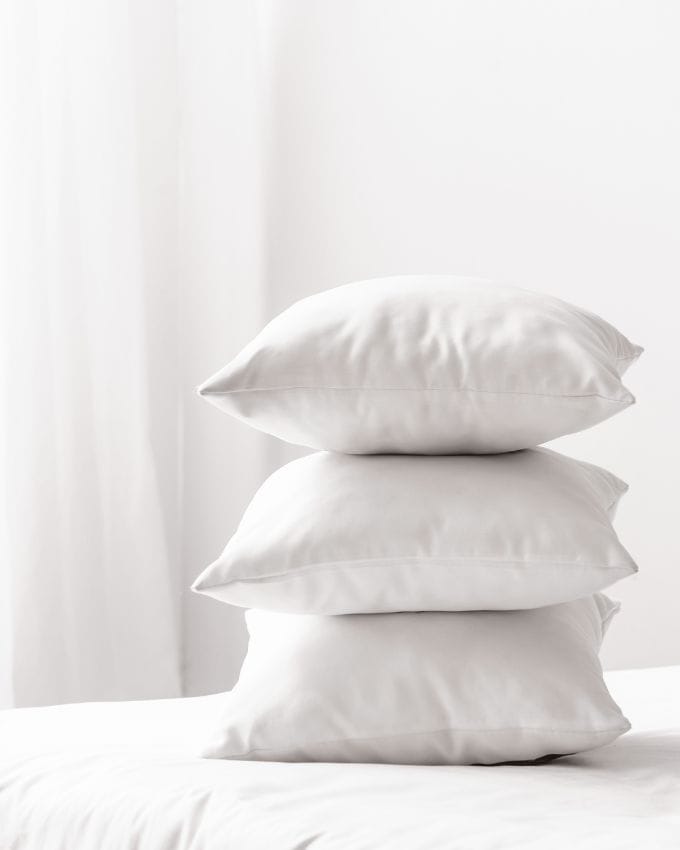 Weiße Kissen auf einem Bett, weißer Vorhang im Hintergrund