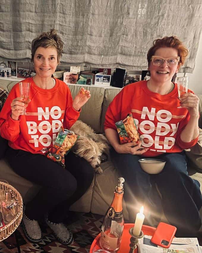 Zwei Frauen in rotem Pullover trinken Sekt und essen Chips