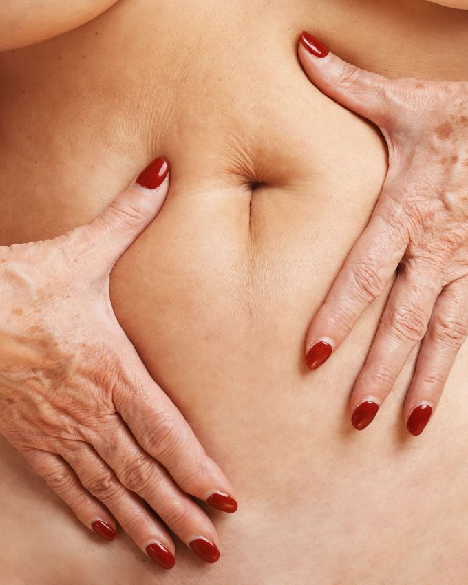 Bauch einer Frau gehalten von den Händen, lackiert mit rotem Nagellack