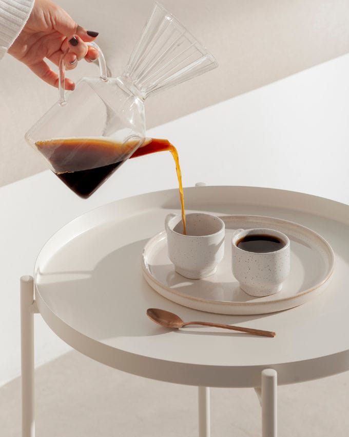 weißer Tisch mit 2 Kaffeetassen, in die Kaffee eingeschenkt wird