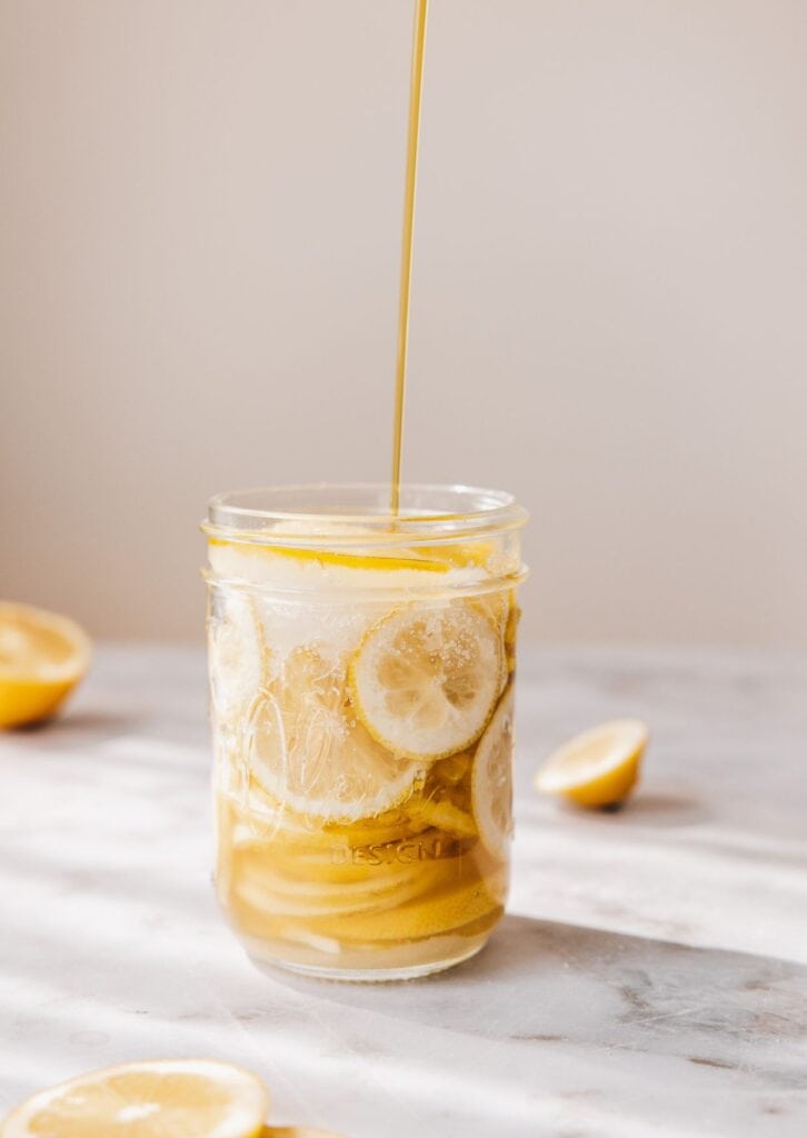 Glas mit fermentierten Zitronenscheiben und Honig auf hellem Marmortisch – natürliche Fermentation für gesunde Ernährung.
