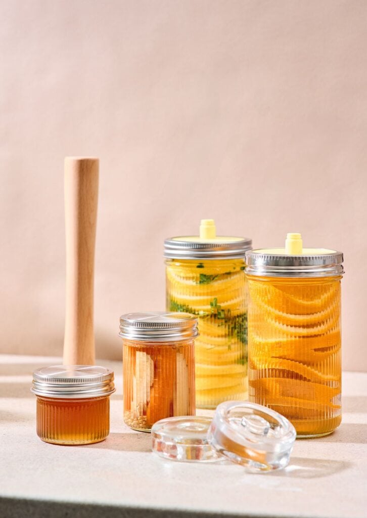 Fermentier-Set mit Gläsern, Holzstampfer und fermentierten Zitronen auf hellem Hintergrund – ideal für natürliche Fermentation zu Hause.