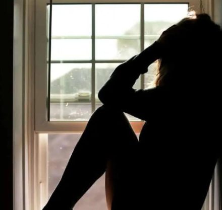 Umriss von Frau sitzt im Fenster und fasst sich an Kopf