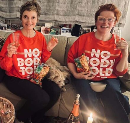 Zwei Frauen in rotem Pullover trinken Sekt und essen Chips