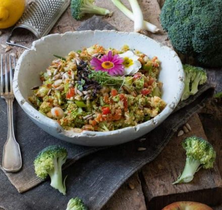 Brokkoli- Apfel- Salat in grauer keramikschale serviert, mit Sprossen und essbaren Blumen garniert.
