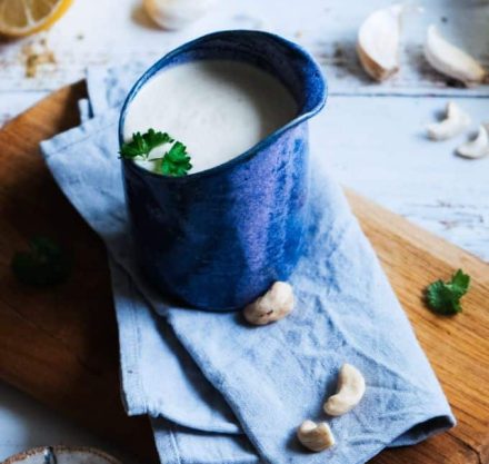 wir sehen ein Glas Cremige Cashew-Sauce auf einem blauen Tuch, das auf einem Holztisch steht