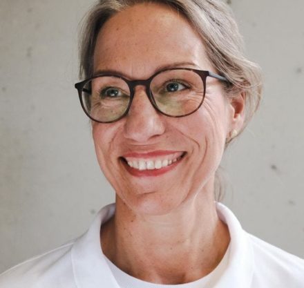 Frau mit blonden Haaren, Brille und weißem Kittel