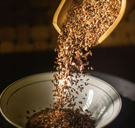 Braune Leinsamen werden aus einer Holzschaufel in eine weiße Schüssel geschüttet.