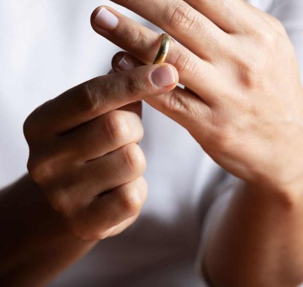 Frau nimmt sich Ehering vom Finger. Die Nägel sind lackiert.