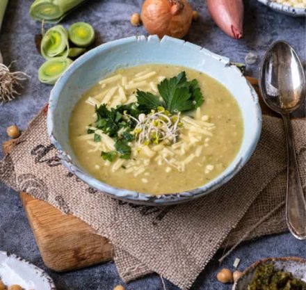 cremige Suppe aus Kichererbsen und Lauch mit frischen Kräutern und veganem Käse garniert