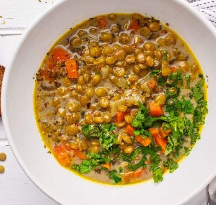 Eine Schüssel mit würziger Linsensuppe, garniert mit frischem Koriander und Karottenstücken, serviert auf einem weißen Hintergrund – perfekt für ein wärmendes und nährstoffreiches Essen.