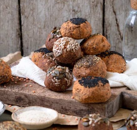 Linsenbrötchen getoppt mit verschiedenen Samen und Kernen, angerichtet auf einem Holzbrett.