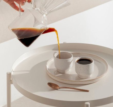weißer Tisch mit 2 Kaffeetassen, in die Kaffee eingeschenkt wird
