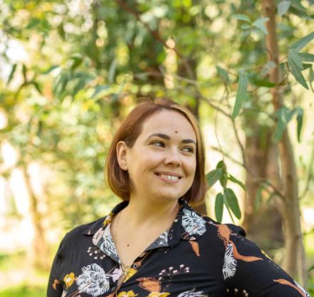 Marisa Tusha smiling with a green tree behind