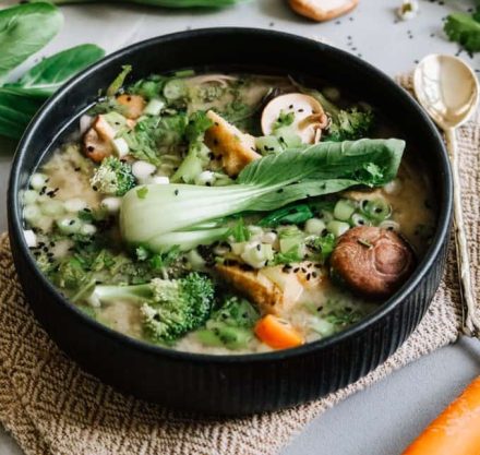 Eine Schale mit Miso und Gemüsesuppe auf einem weißen Tuch. Auf dem Tisch sind Karotten und Gemüse drum herum zu sehen