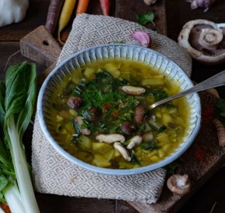 Pilzsuppe in blauer Schüssel mit Karotten, Sellerie und gelber Beete. Garniert mit frischer Petersilie.