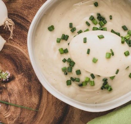 Cremige Blumenkohlsuppe garniert mit Schnittlauch, serviert in einer weißen Schüssel auf rustikalem Untergrund.