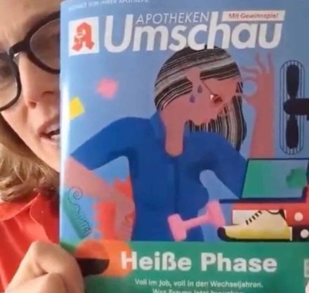 Frau mit großer Brille hält Zeitschrift in die Kamera.