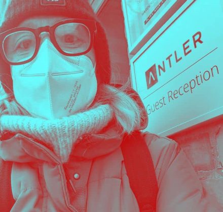 Frau mit Brille, Mütze und Maske in Winterjacke und Rollkragenpullover.