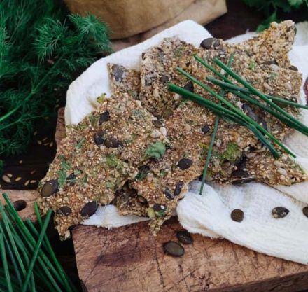 Seed cracker auf einem weißen Tuch und einem Holzbrett. Um das Brett herum ist Gemüse zu sehen.