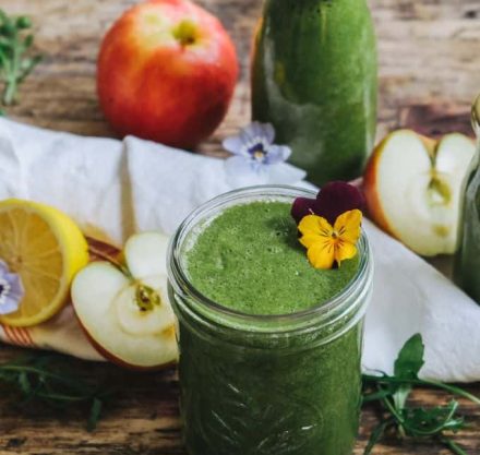Grüner Smoothie im Glas mit Blättern und Äpfeln und Zitrone drumherum