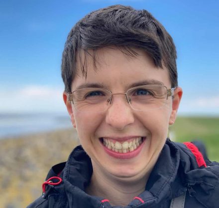 Eine junge Frau mit kurzen Haaren, Brille und dunkelblauer Windjacke