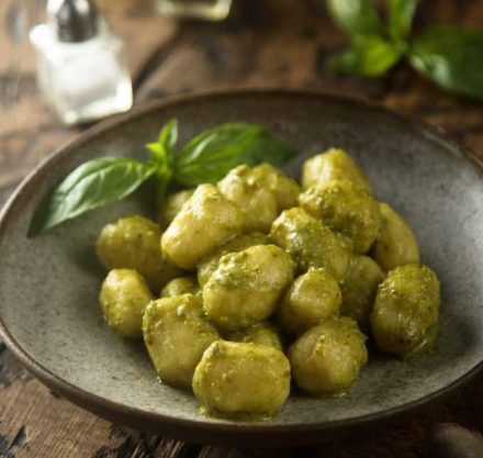 Tofu Gnocchi mit grünem Pesto auf grauem Teller serviert, garniert mit Basilikum.