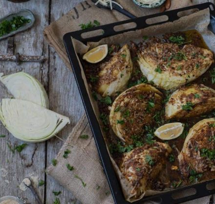 Mit veganem Parmesan überbackene Weißkohlspalten auf einem Backblech angerichtet und mit Petersilie garniert.