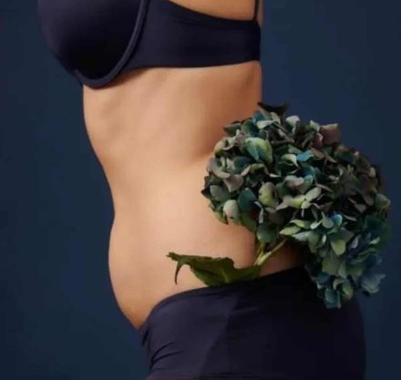 Frau in schwarzer Unterwäsche mit dunkler Blume und schwarzem Hintergrund