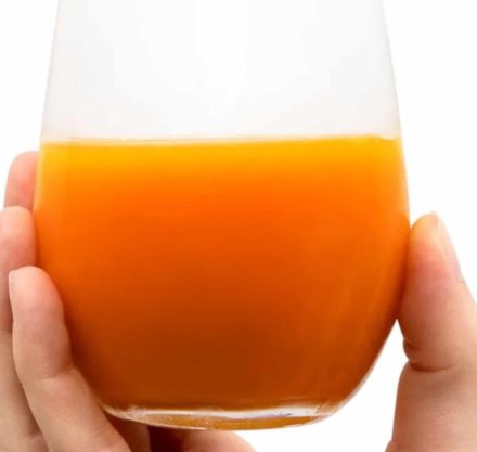 Eine Hand hält ein Glas mit orangefarbenem LaVita Mikronährstoffkonzentrat